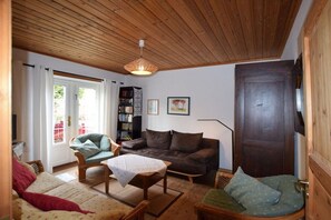 A cozy living room with a wooden ceiling, a sofa, a chair, a small table, and a bookshelf. - ||-------------------1 in the House of the Wren------------------|| (Prerow)