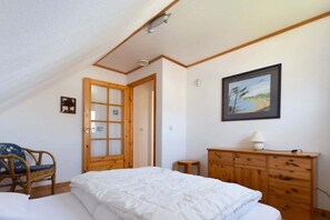 A bedroom with a bed, wooden dresser, a chair, a door, and a framed picture on the wall. - Holiday home in Prerow with swimming pool (Prerow)