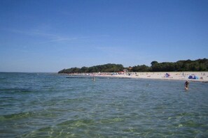 A beach with clear water, a sandy shore, and a forested hill in the background. - Holiday home with 1 bedroom (Insel Poel - OT Kaltenhof)