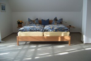 Ein Bett mit einem gemusterten Überwurf, ein Nachttisch mit einer Lampe und ein Topf mit einer Pflanze auf dem Beistelltisch.