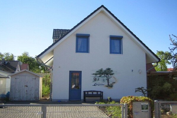 A two-story house with a blue door, a small porch with a bench, and a mural of a tree on the front wall. - Holiday home with 1 bedroom (Insel Poel - OT Kaltenhof)
