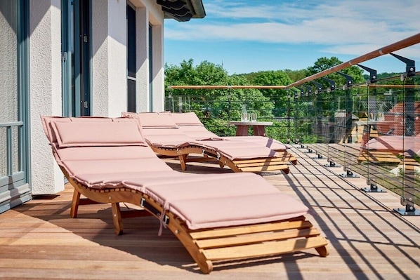 A wooden deck with lounge chairs and a table, overlooking a garden.