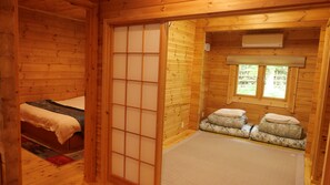 A traditional Japanese-style room with tatami flooring, a sliding shoji screen, a bed with a futon, and a small seating area with cushions.