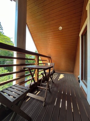 A wooden deck with a sloped ceiling, outdoor seating, and a view of greenery.
