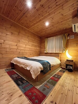 A wooden cabin bedroom with a bed, a nightstand, a lamp, and a window with curtains.