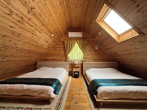A cozy attic bedroom with two beds, a skylight, and a small bedside table with a lamp.