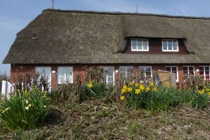Ein Haus mit einem Reetdach, einer Backsteinfassade, mehreren Fenstern und einem Garten mit gelben Blumen.