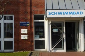 A building entrance with a sign reading 'SCHWIMMBAD' and a Nationalparkhaus sign. - "Hygge" - a thatched-roof house (Nordstrand)