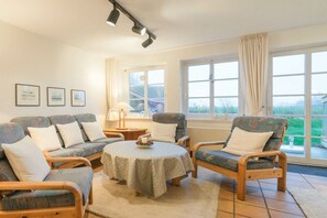 A living room with a sofa set, a round table, and a view of the outdoors through large windows. - "Hygge" - a thatched-roof house (Nordstrand)