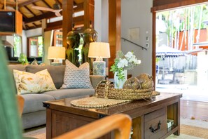 A living room with a sofa, lamps, a woven basket, and a vase with flowers. - Far Pavilions - An Intimate Bali-style Haven (Port Douglas)