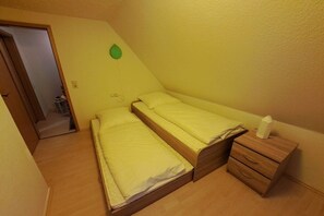 A small room with two single beds, a wooden nightstand, and a green leaf decoration on the wall. - Relaxation under a thatched roof (Bordelum\/Sterdebüll)