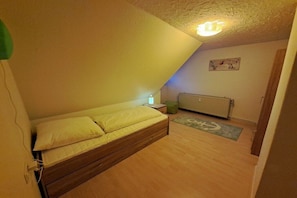 A bedroom with a single bed, a nightstand, a radiator, and a small rug. - Relaxation under a thatched roof (Bordelum\/Sterdebüll)