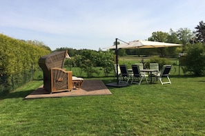Ein Außenbereich mit Sitzgelegenheiten, einem Tisch, Stühlen und einem großen Sonnenschirm, sowie einem einzigartigen Skulpturelement.