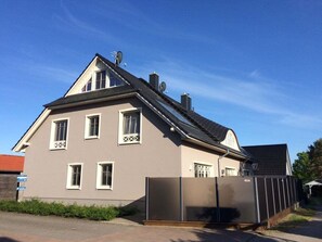Ein zweistöckiges Haus mit geneigtem Dach, Satellitenschüsseln und einem von einem Tor gesäumten Auffahrt.