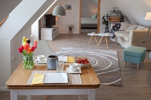 A dining area with a wooden table set for two, a vase of tulips, and a bowl of strawberries. - Holiday apartment with 1 bedroom (Gelting)