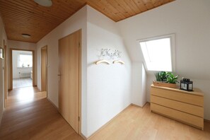 A hallway with wooden flooring, a wooden ceiling, a wooden door, a wall-mounted coat rack, a window with a view, and a wooden dresser with a plant and a lantern. - Holiday apartment in Rade with barbecue (Rade)