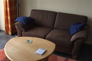 En brun soffa med blå kuddar, ett träbord och en röd matta.