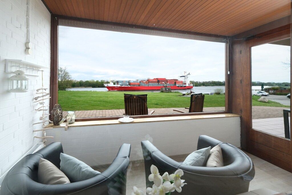 Ein Zimmer mit Blick auf einen Fluss und ein rotes Boot, ausgestattet mit zwei grauen Sofas und einem kleinen Tisch.