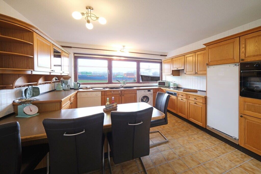 A kitchen with wooden cabinets, a dining table with chairs, a washing machine, and a refrigerator.