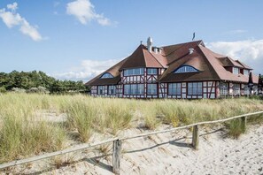 A traditional half-timbered building with a sloped roof, situated on a sandy beach with a wooden fence in the foreground. - Holiday apartment with 1 bedroom (Zingst)