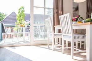 A room with a sliding glass door leading to a balcony, white furniture, and a table with a vase of flowers. - Holiday apartment with 1 bedroom (Zingst)