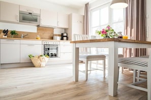 A modern kitchen with white cabinetry, a wooden countertop, and a dining area with striped chairs. - Holiday apartment with 1 bedroom (Zingst)