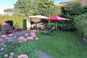 Eine Gartenpatio mit Tisch, Stühlen und einem roten Sonnenschirm.