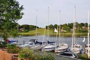 A marina with multiple sailboats docked, surrounded by greenery and a calm water body. - Holiday home with 2 bedrooms (Brodersby)