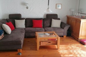 Ein Wohnzimmer mit einer Sofagarnitur, einem Glastisch und einem Holzschrank.