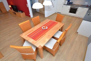 Eine moderne Küche mit weißen Schränken, einem eingebauten Backofen und einem Essbereich mit Holztisch und Korbstühlen.