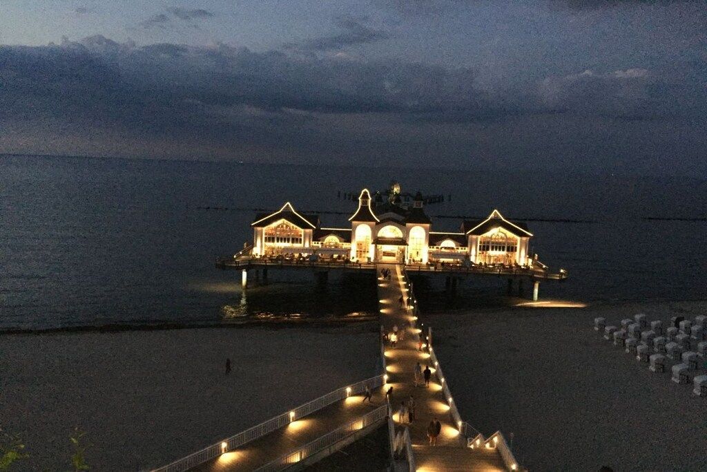 Een hotel aan het water met een lange steiger die naar het gebouw leidt, met meerdere verlichte constructies.