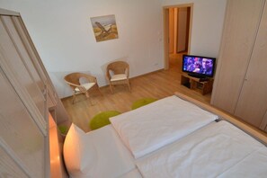 Een slaapkamer met een bed, een televisie, een stoel en een schilderij aan de muur.
