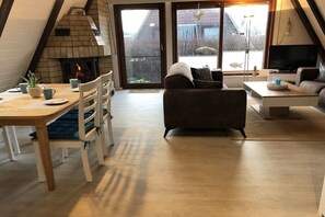 A cozy living room with a fireplace, a dining area, and a seating area with a television. - Holiday home with 2 bedrooms (Friedrichskoog)