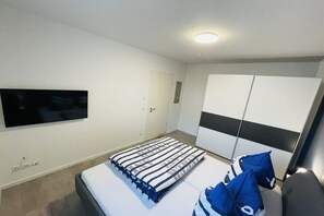 A bedroom with a bed, a television mounted on the wall, a wardrobe, and a door. - Baltic Sea anchorage (Rostock)