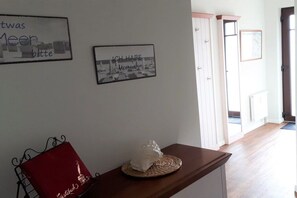 Un pasillo con un banco de madera, una silla roja y dos cuadros en la pared.