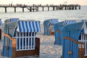 Sillas de playa junto a la orilla, con números, un muelle al fondo y una playa arenosa.