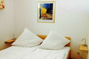A room with a bed, two white pillows, a nightstand with a lamp, and a framed picture on the wall. - Residence Am Kurpark (Warnemünde)