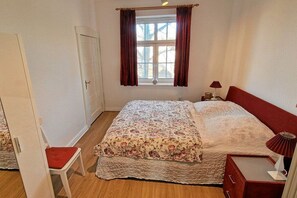 Ein Schlafzimmer mit einem Bett, einem Nachttisch, einer Lampe, einem Fenster mit Vorhängen und einer Tür.