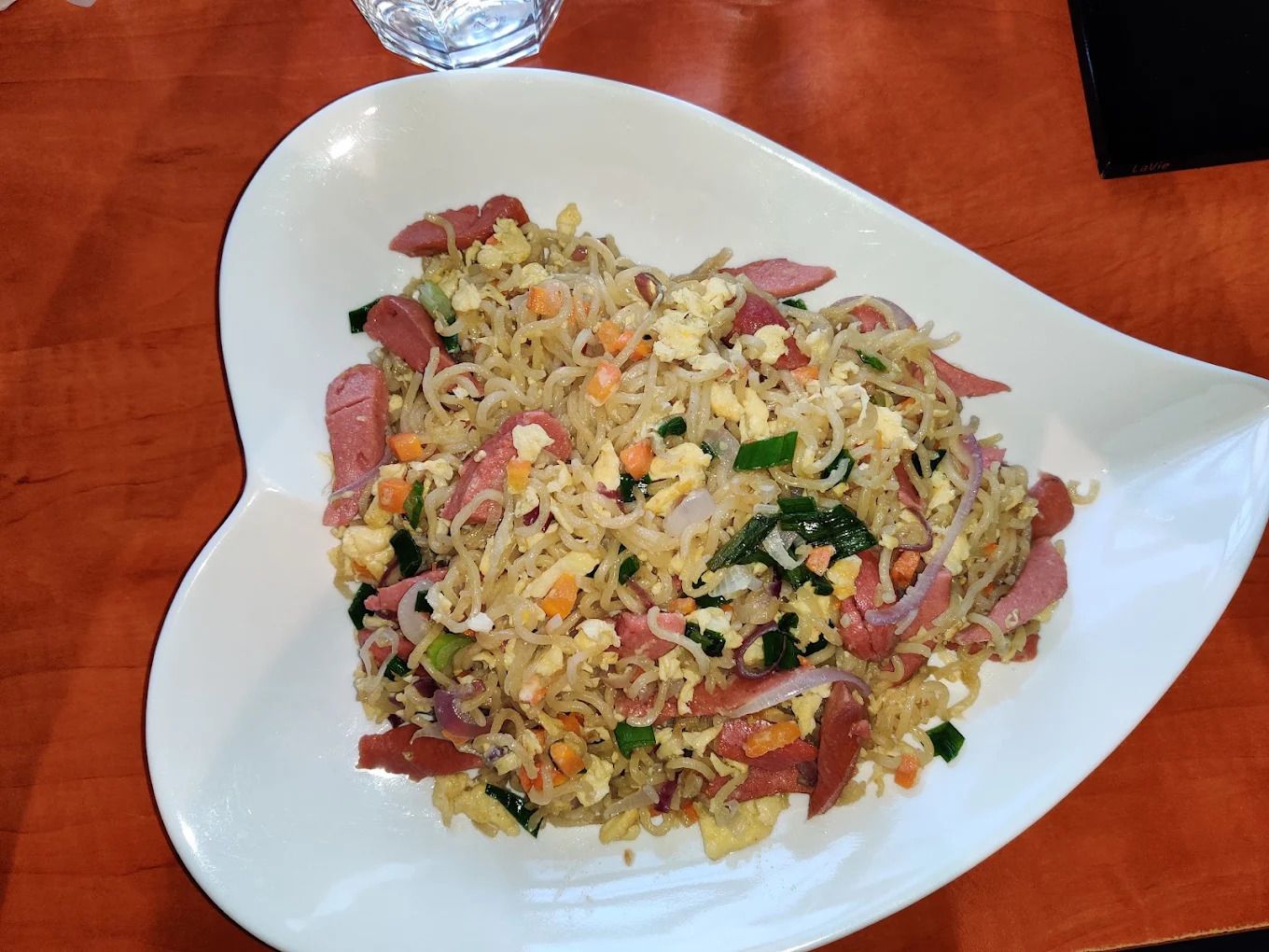 A white plate with a stir-fried dish containing vegetables and meat, placed on a wooden table.