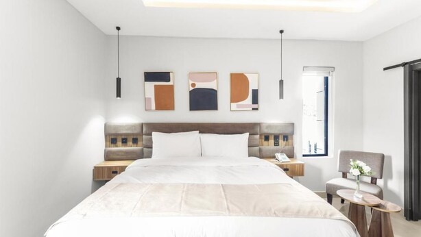 Une chambre d’hôtel moderne avec un grand lit, des tables de chevet, une chaise et des œuvres d’art accrochées au mur.