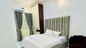 Une chambre moderne avec un grand lit, un fauteuil de couleur sombre et un climatiseur fixé au mur.