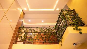 Uma escadaria com corrimão decorado com trepadeiras verdes, teto com iluminação embutida e uma câmera de segurança fixada na parede.