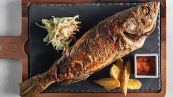 A whole grilled fish with a side of coleslaw and wedges on a slate serving board.
