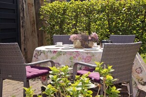 An outdoor dining area with wicker chairs and a table set with white cups and a vase of flowers. - Holiday apartment Luzie (Büsum)
