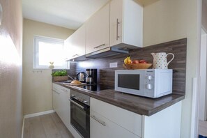 A compact kitchen with a microwave, oven, and a fruit bowl on the counter. - Holiday apartment Luzie (Büsum)