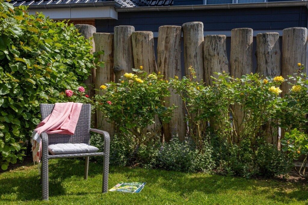Un jardin avec une clôture en bois, une chaise avec une couverture et des plantes en fleurs.