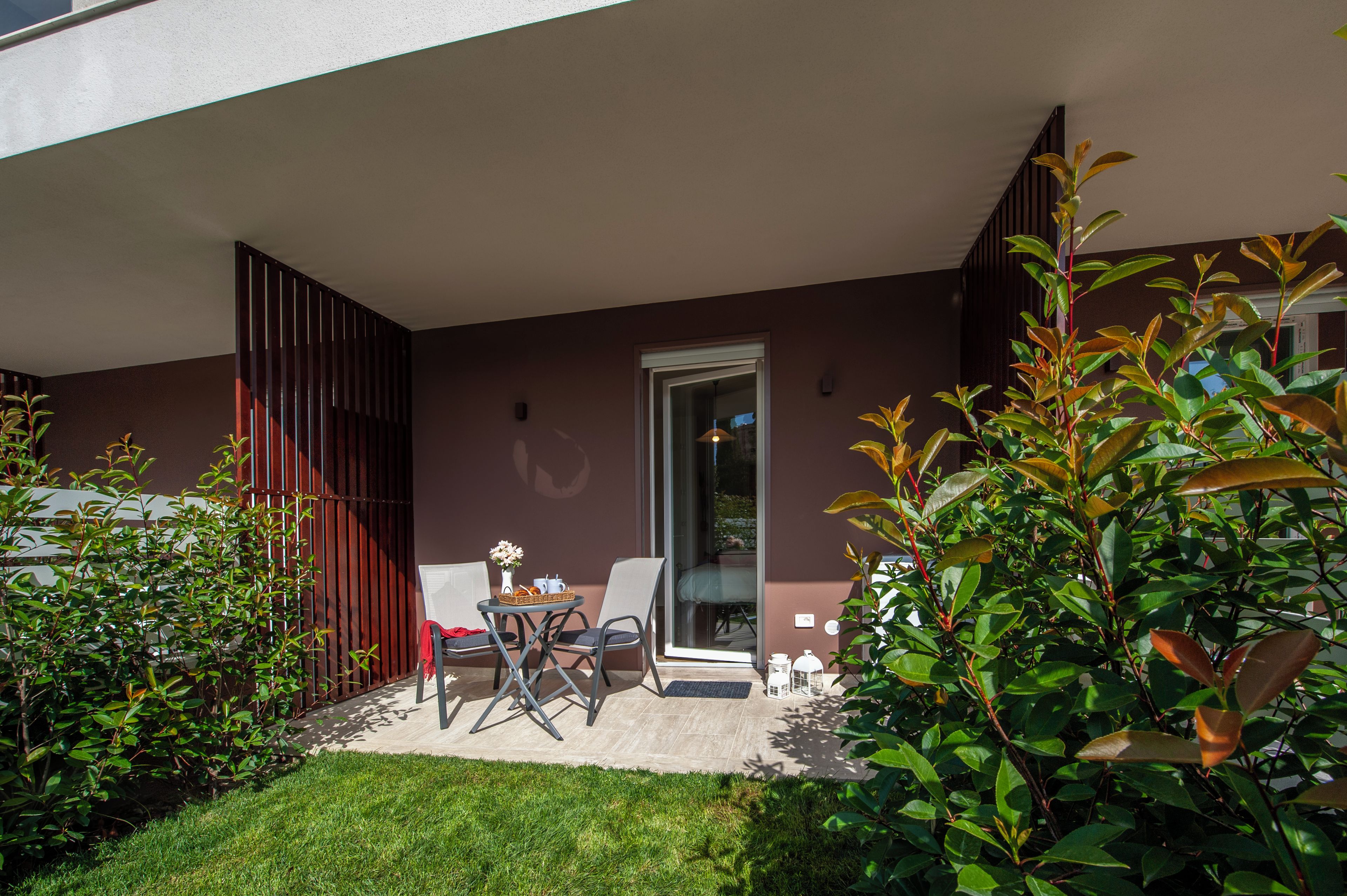 Eine moderne Terrasse im Freien mit Tisch und Stühlen, einem Glastür-Eingang und einem gepflegten Rasen.