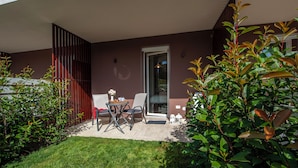 Um pátio moderno ao ar livre com mesa e cadeiras, porta de vidro e gramado bem cuidado.
