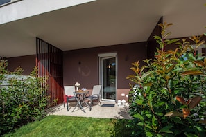 Eine moderne Terrasse im Freien mit Tisch und Stühlen, einem Glastür-Eingang und einem gepflegten Rasen.