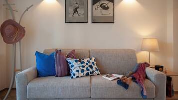 A living room with a sofa, pillows, a floor lamp, and two framed pictures on the wall.